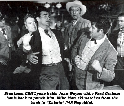 Stuntman Cliff Lyons hold John Wayne while Fred Graham hauls back to punch him. Mike Mazurki watches from the back in "Dakota" ('45 Republic).