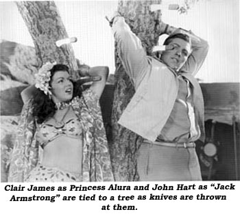 Clair James as Princess Aluna and John Hart as "Jack Armstrong" are tied to a tree as knives are thrown at them.