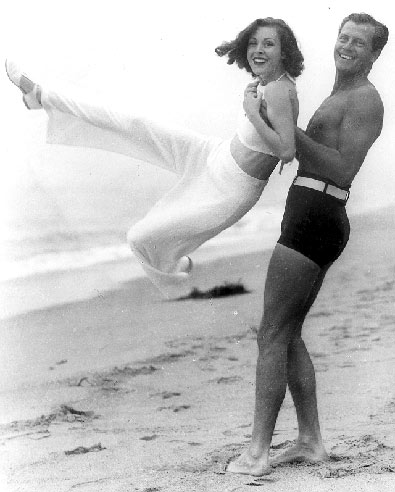 Western star Joel McCrea and his wife Frances Dee cavort on a California beach. Circa 1950's.