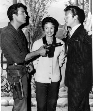 “Whadda mean, you’re gonna be a Maverick cousin?” wonders Ty “Bronco” Hardin to Roger Moore. Andrea Martin smiles in the middle. 