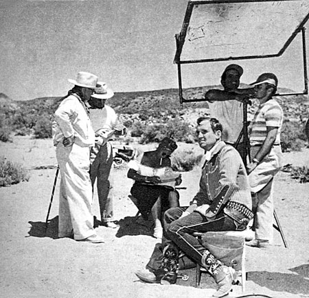 Gene Autry takes a break while technicians make ready for his next scene.