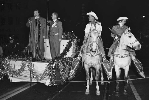 Roy Rogers and Dale Evans on Trigger and Buttermilk await the start of the 1951 Santa Claus Lane Parade in Hollywood while comedian Red Skelton and chairman William Parker kick off the ceremonies.