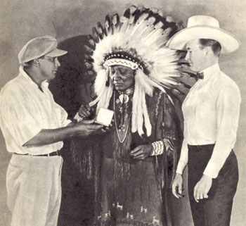 Tim McCoy looks on while director James Cruze makes a presentation to one of the Indian Chiefs who appeared in “The Covered Wagon” (‘23).