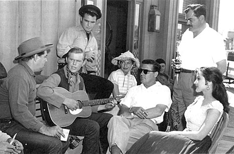 Relaxing between scenes of TV’s “Riverboat” are (L-R) John Mitchum, singer Rusty Richards, Burt Reynolds, woman (name unknown) choreographer for that episode of the series, director Dick Bartlett, scriptwriter Norm Jolley and guest star Debra Paget. 