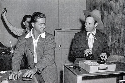 Creating Gene Autry’s radio show. A sound effects man uses the old reliable coconut shells to keep up with the hooves of Champion achieved by Gene himself. Note the door behind Gene which is used for everything from entering and exiting the front door of a cabin to entering and exiting Gene's office. Also note the turntable at the left for “needle-drop” sound effects and the other sound effects man holding a gun in the air. 