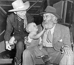 Roy Rogers smiles as his young son Dusty takes a tug at Gabby Hayes’ beard. 