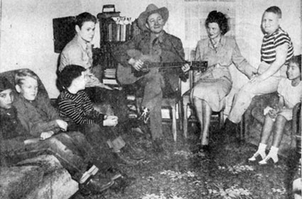 Tex Ritter took time out from his personal appearances at the Kimo Theatre to entertain physically handicapped homebound children who could not attend public schools. Photo March 21, 1948 at the home of Mrs. W. Hastings in Albuquerque, New Mexico. May Porter, the children's teacher is to the left of Tex. 