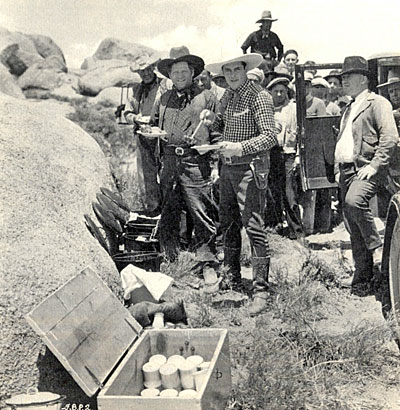 Ken Maynard and veteran heavy Fred Kohler take time out for lunch while on location in Lone Pine, CA, during the filming of “Fiddlin’ Buckaroo” (‘33 Universal). Peeking out of the car at the extreme right is the owner of Lone Pine’s Anchor Ranch, Russ Spainhower. 