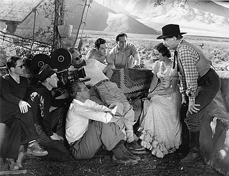 Director Lesley Selander (white shirt seated on the ground) directs Evelyn Venable and Robert Barrat in a scene for Paramount’s “Heritage of the Desert” (‘39) while several crew members and star Donald Woods (center) look on. 