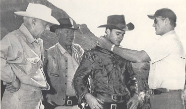 On the set of “Rio Bravo” director Howard Hawks and Ward Bond observe as John Wayne puts a finishing touch on Ricky Nelson’s costume which is a slightly modified version of the jacket worn by Montgomery Clift in “Red River”. 