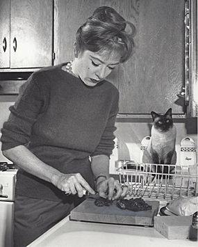 A very domestic Miss Kitty...Amanda Blake...prepares dinner while another “kitty” looks on. 