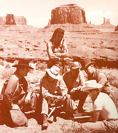 While talking over the making of a scene for “The Searchers” (‘55) in Monument Valley, Utah, an Indian actor stands beside (L-R) John Wayne, director John Ford, Harry Goulding, Ward Bond and a man holding the script. 