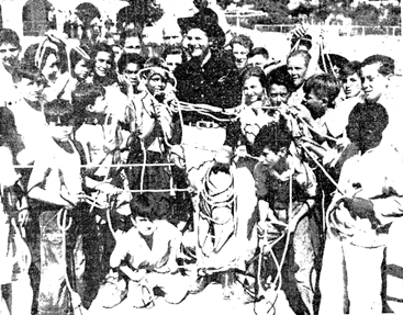 Rex Bell gives instruction to a group of boys from L.A. playgrounds on the art of roping when they visited him at his Walking Box San Fernando ranch. Six boys were selected to take part in a rodeo roping contest. The winners were later given a two week vacation at Bell's ranch.