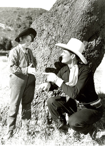 Charles Starrett and Delmar Watson discuss their scenes in an offscreen moment from “Outlaws of the Prairie” (‘37 Columbia). This Starrett film contains the most bloodthirsty, brutal scene in B-western history. Excruciating to watch, it’s amazing the scene made it past the censors. Two outlaws (Lambert Rogers, Dick Alexander) shoot and kill Starrett’s father while he watches as a young boy (Delmar Watson). He wings one of them in the arm with his rifle, then Rogers viciously cuts two fingers off the boy’s right hand with a hunting knife while the boy screams in pain. Rogers literally adds insult to injury and kicks the devastated boy leaving him crying and screaming in pain. Full grown, now a Texas Ranger, Starrett searches the West for the killer and eventually finds him.