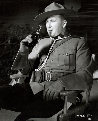 And now, to wind this page up, let’s enjoy the pause that refreshes as Tim McCoy sips a Coke during a break from the filming of “Fighting Shadows” (‘35 Columbia).