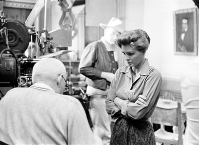 Angie Dickinson discusses her “Rio Bravo” script with director Howard Hawks. Note in the first photo John Wayne is mostly obscured by the camera, but by the second photo he has walked into the background.