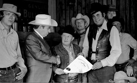 (L-R) Bill Wright, cartoonist Max Harrison, Tex Barr, Leonard Worth, Sunset Carson, Bill Riley and Jesse Baker during the making of “Marshal of Windy Hollow”. Max is presenting Tex Barr with the Kentucky Colonel certificate.