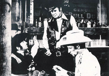 Sunset Carson holds a gun on Glenn Huffman (L) and Leonard Mann (R) in the saloon from “Marshal of Windy Hollow”.