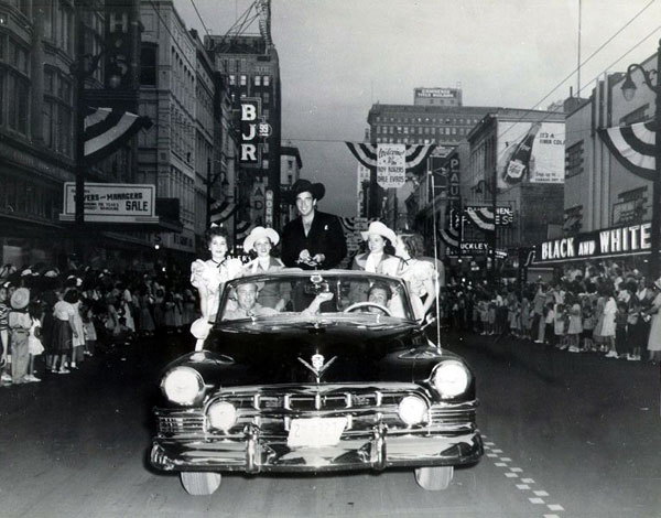 Lash LaRue and a bevy of cowgirls ride in a Paterson, NJ, parade. Date unknown but note the Welcome to Roy Rogers, Dale Evans banner in the background. (Thanx to Jerry Whittington.)
