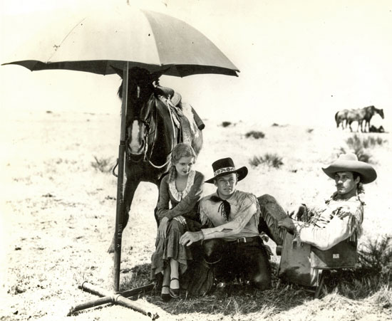 Getting out of the sun, Lucile Browne, Rex Bell and Tom Tyler wait for the next scene of “Battling with Buffalo Bill” (‘31 Universal serial).