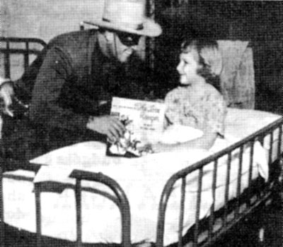 Clayton Moore talks with a crippled child and presents her with a Lone Ranger record at the New Orleans Charity Hospital on February 4, 1956.