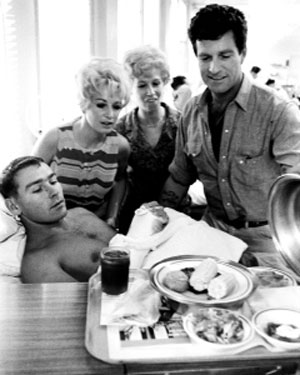 Hugh O’Brian, TV’s “Wyatt Earp”, unveils dinner in July 1967 for Marine Sgt. William Ferrell, a patient at Yokosuka Naval hospital. He was wounded the previous month at Dong Ha, Viet Nam. Behind them are Linda Michele and Ruth Lawrence of the U.S.O.’s “Guys and Dolls” dance troupe.