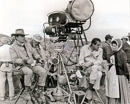 John Wayne sits idly by as director Andrew McLaglen provides some direction to Yvonne De Carlo on the set of “McLintock!” (‘63).