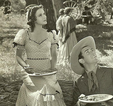 Pausing to look up at someone while eating lunch on location are Johnny Mack Brown and leading lady ???