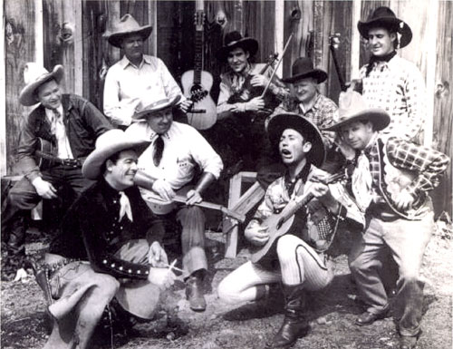Range Riders singing group circa 1934-‘35. (L-R back row) Jack Kirk, unknown standing, possibly Ace Spriggins, Hilo Pete McKinney (white shirt with guitar sitting, Oscar Gahan, unknown, Jack Jones. (L-R front row) Glenn Strange, Cactus Mack McPeters, Loyal Underwood.