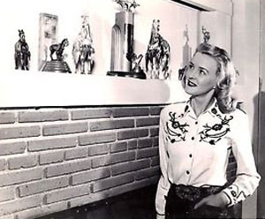 Rodeo queen and Monogram B-Western leading lady Reno Browne looks at some of her many rodeo trophies.