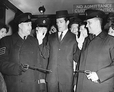 Hugh “Wyatt Earp” O’Brian, arriving at Heathrow Airport in 1958, is disarmed of his Buntline Special and sixgun by London Customs officials. (Thanx to Terry Cutts.)