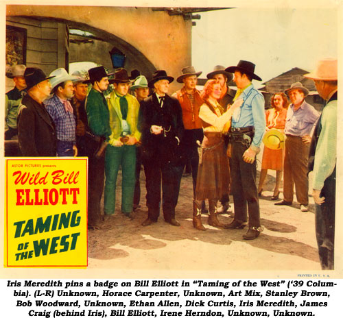 Iris Meredith pins a badge on Bill Elliott in "Taming of the West" ('39 Columbia). (L-R) Unknown, Horace Carpenter, Unknown, Art Mix, Stanley Brown, Bob Woodward, Unknown, Ethan Allen, Dick Curtis, Iris Meredith, James Craig (behind Iris), Bill Elliott, Irene Herndon, Unknown, Unknown.