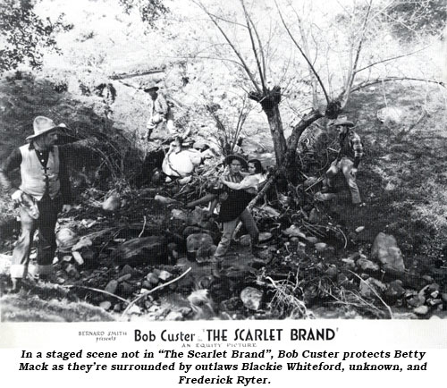 In a staged scene not in "The Scarlet Brand", Bob Custer protects Betty Mack as they're surrounded by outlaws Blackie Whiteford, unknown, and Frederick Ryter.